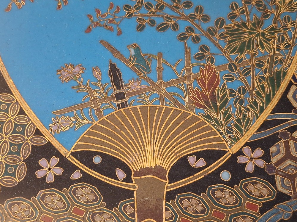 A circular Japanese Meiji period cloisonne charger featuring a sky-blue central medallion with chrysanthemums, a butterfly, and a frog, framed by geometric enamel patterns. View XI