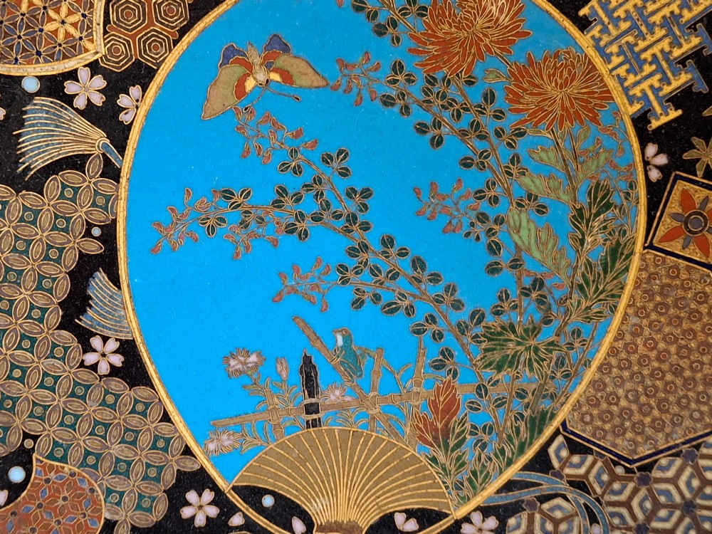 A circular Japanese Meiji period cloisonne charger featuring a sky-blue central medallion with chrysanthemums, a butterfly, and a frog, framed by geometric enamel patterns. View XII