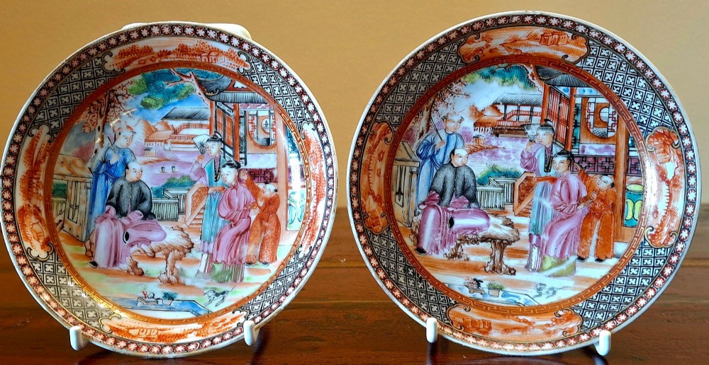 A set of four circular Chinese export porcelain saucers hand-painted with figural scenes inside pavilions framed by geometric borders in orange and polychrome enamels.