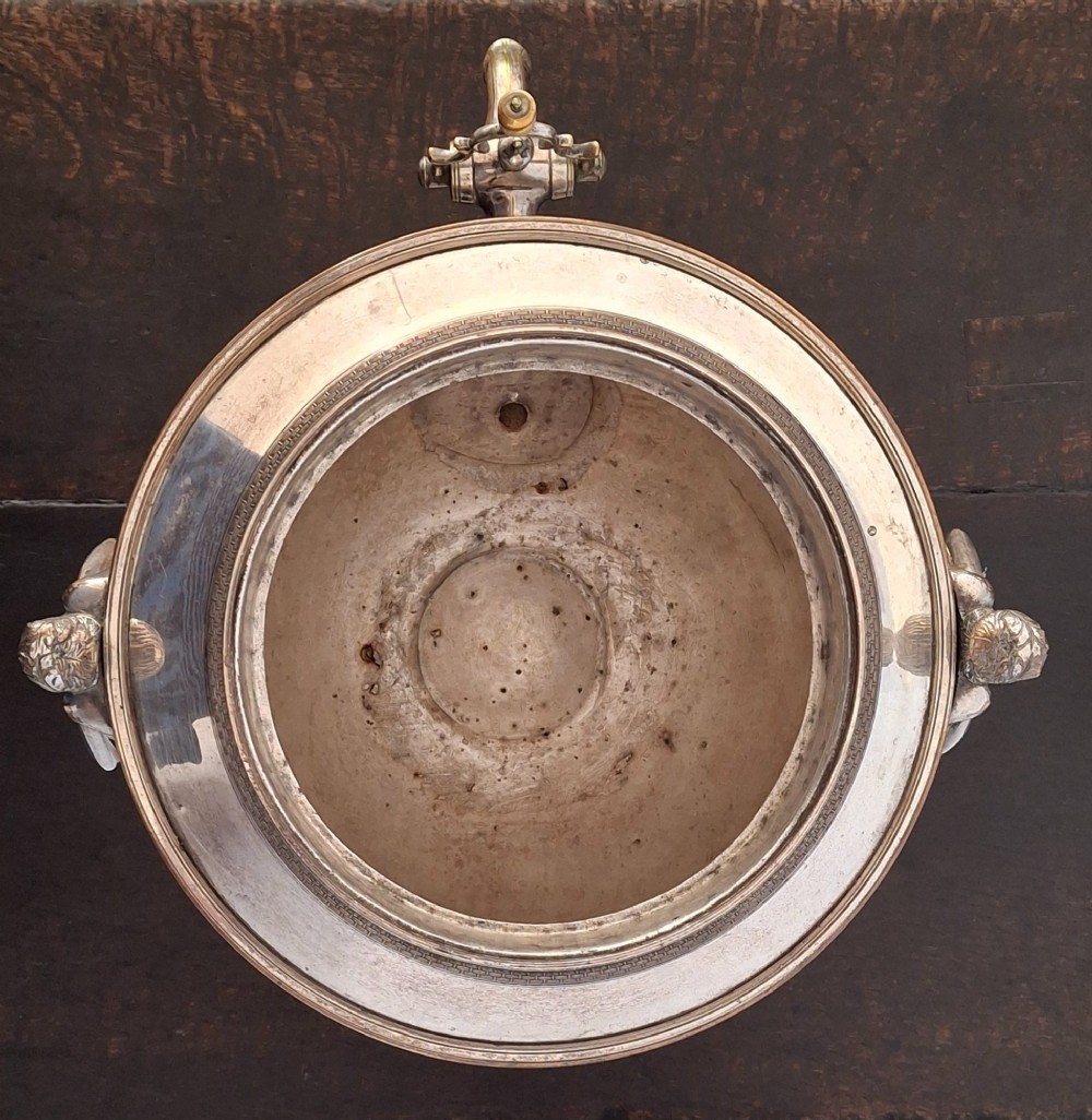 An antique silver-plated Regency tea urn featuring a top dolphin finial, classical figure side handles, a front spigot, and a square base supported by ball feet. View XIV