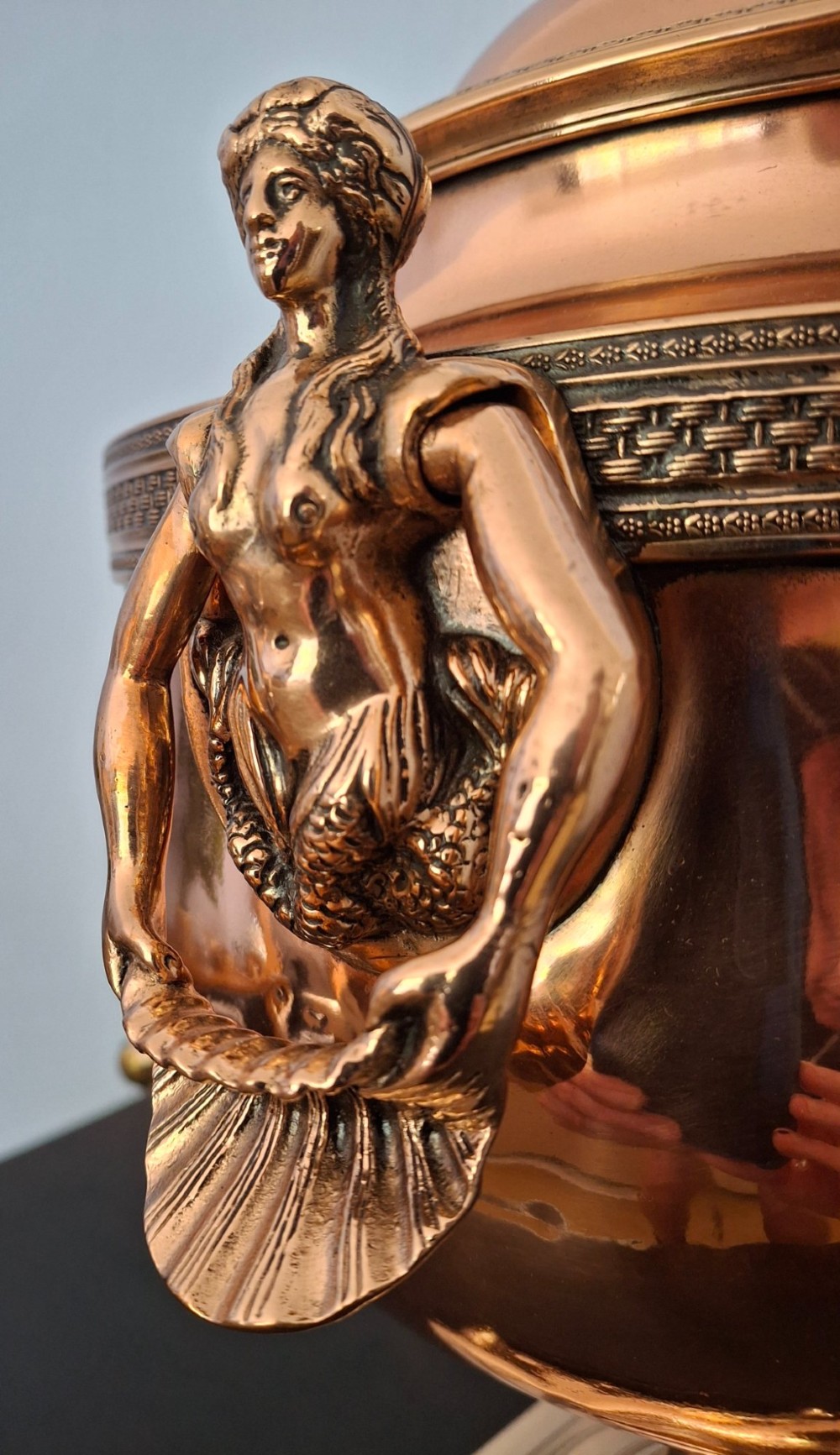 An antique polished copper and brass tea urn featuring a urn-shaped body, crest finial, side handles, and a spigot, resting on a square pedestal base. View VII