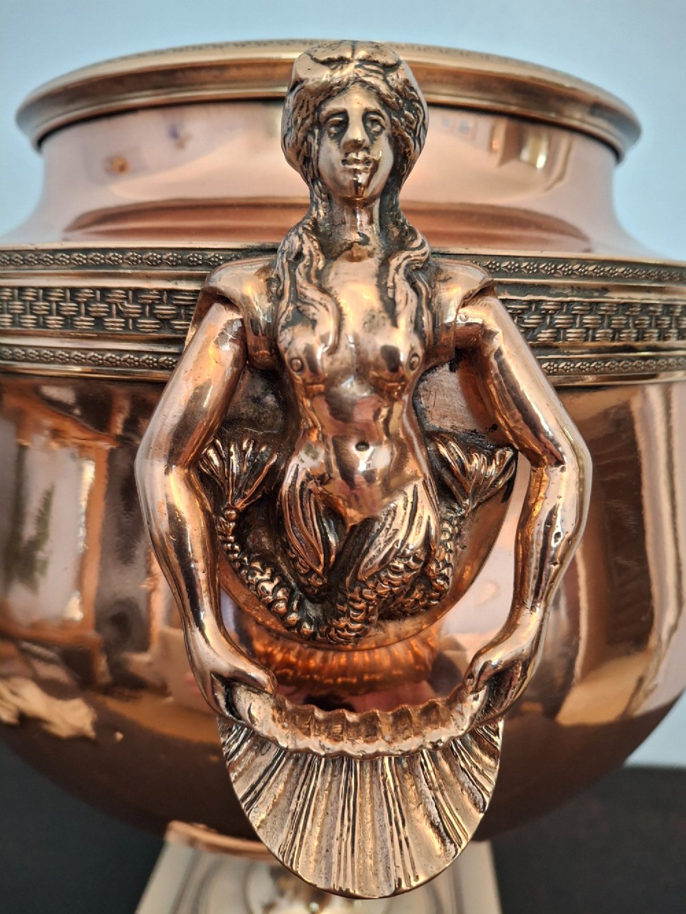 An antique polished copper and brass tea urn featuring a urn-shaped body, crest finial, side handles, and a spigot, resting on a square pedestal base. View XIII