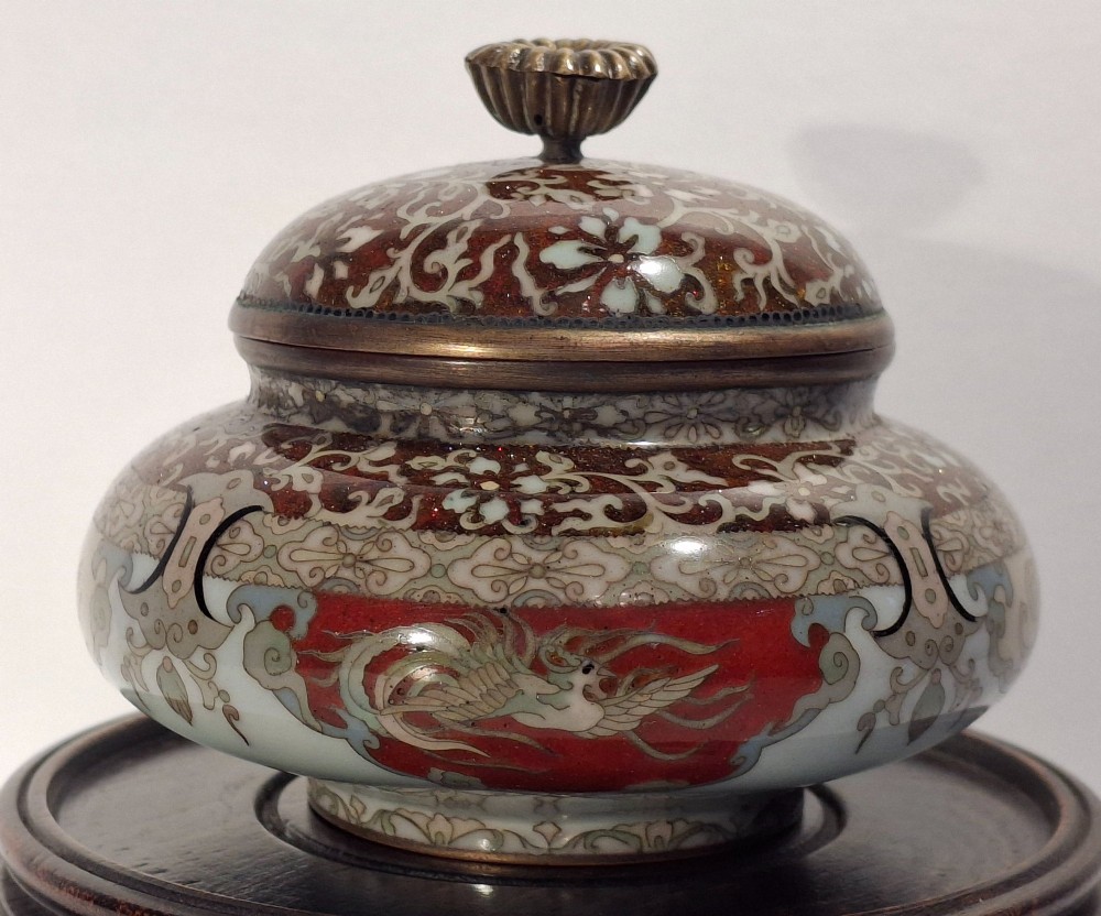 A Japanese cloisonne enamel koro decorated with phoenix motifs and intricate floral scrollwork, topped with a domed lid and carved finial.