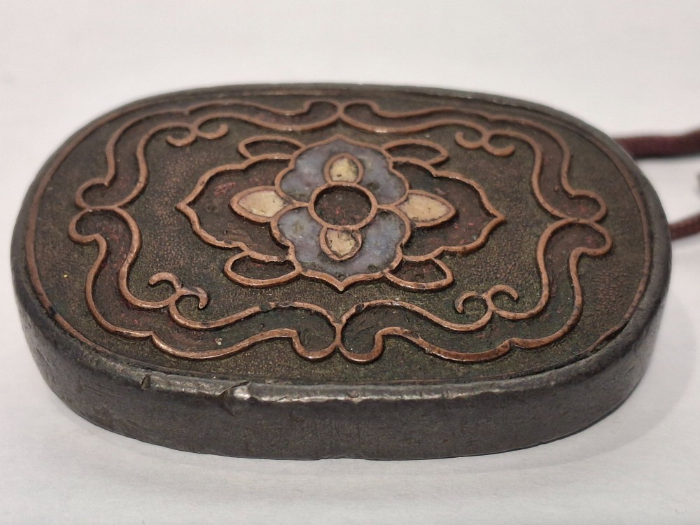 An oval-shaped pewter Japanese manju netsuke featuring champleve enamel floral decoration and an attached cord. View II