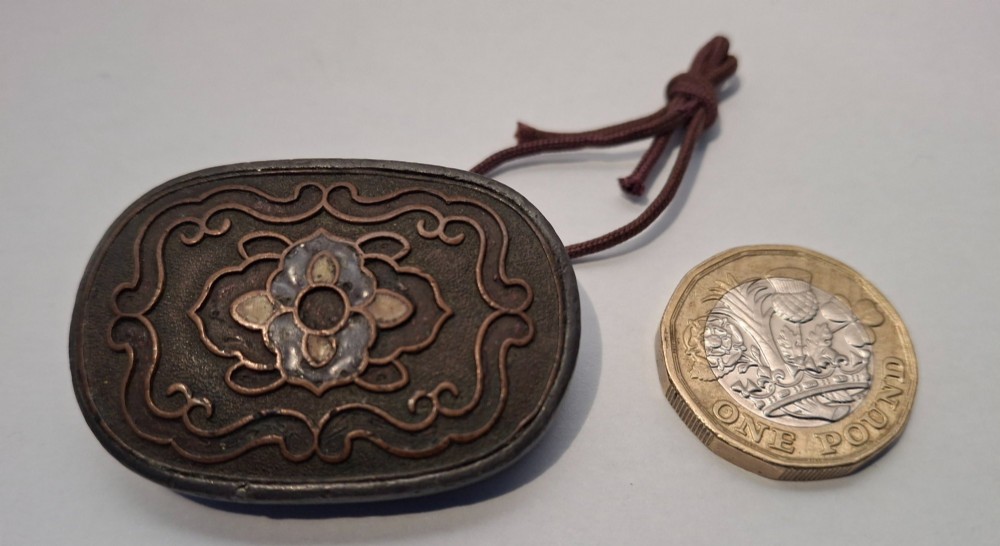 An oval-shaped pewter Japanese manju netsuke featuring champleve enamel floral decoration and an attached cord. View V