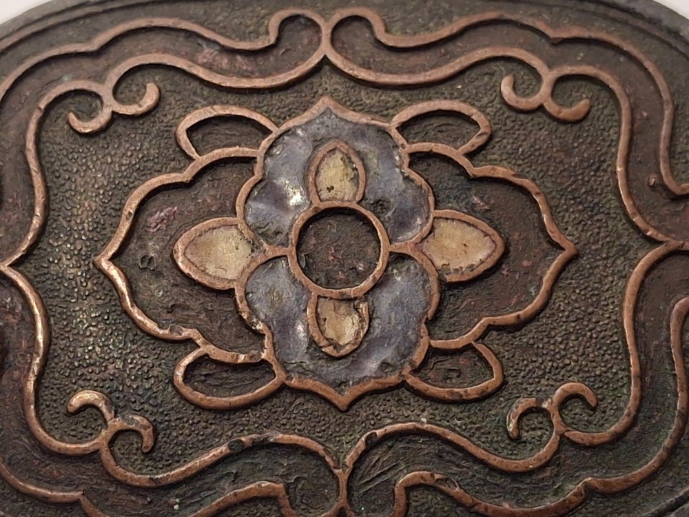 An oval-shaped pewter Japanese manju netsuke featuring champleve enamel floral decoration and an attached cord. View X