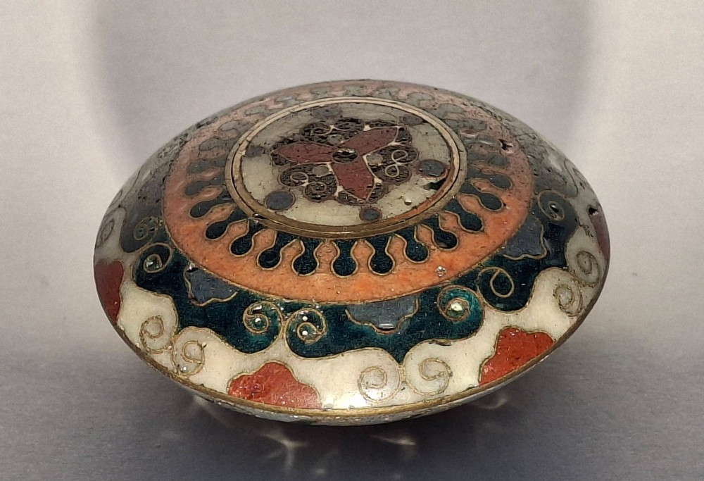 A circular Japanese manju netsuke in polychrome cloisonne enamel with central floral medallion and spiral border patterns. View II