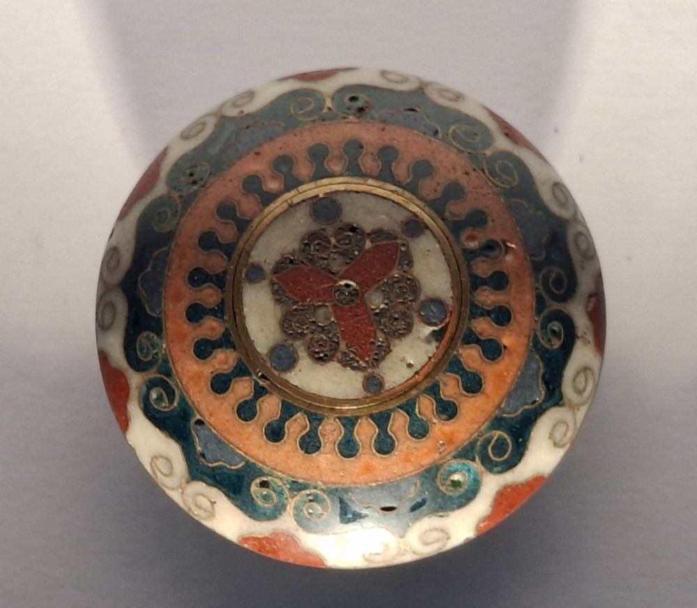 A circular Japanese manju netsuke in polychrome cloisonne enamel with central floral medallion and spiral border patterns. View III
