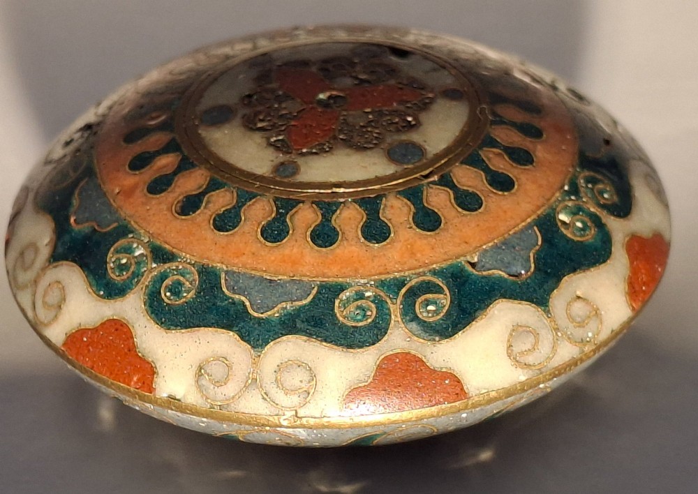 A circular Japanese manju netsuke in polychrome cloisonne enamel with central floral medallion and spiral border patterns. View IV