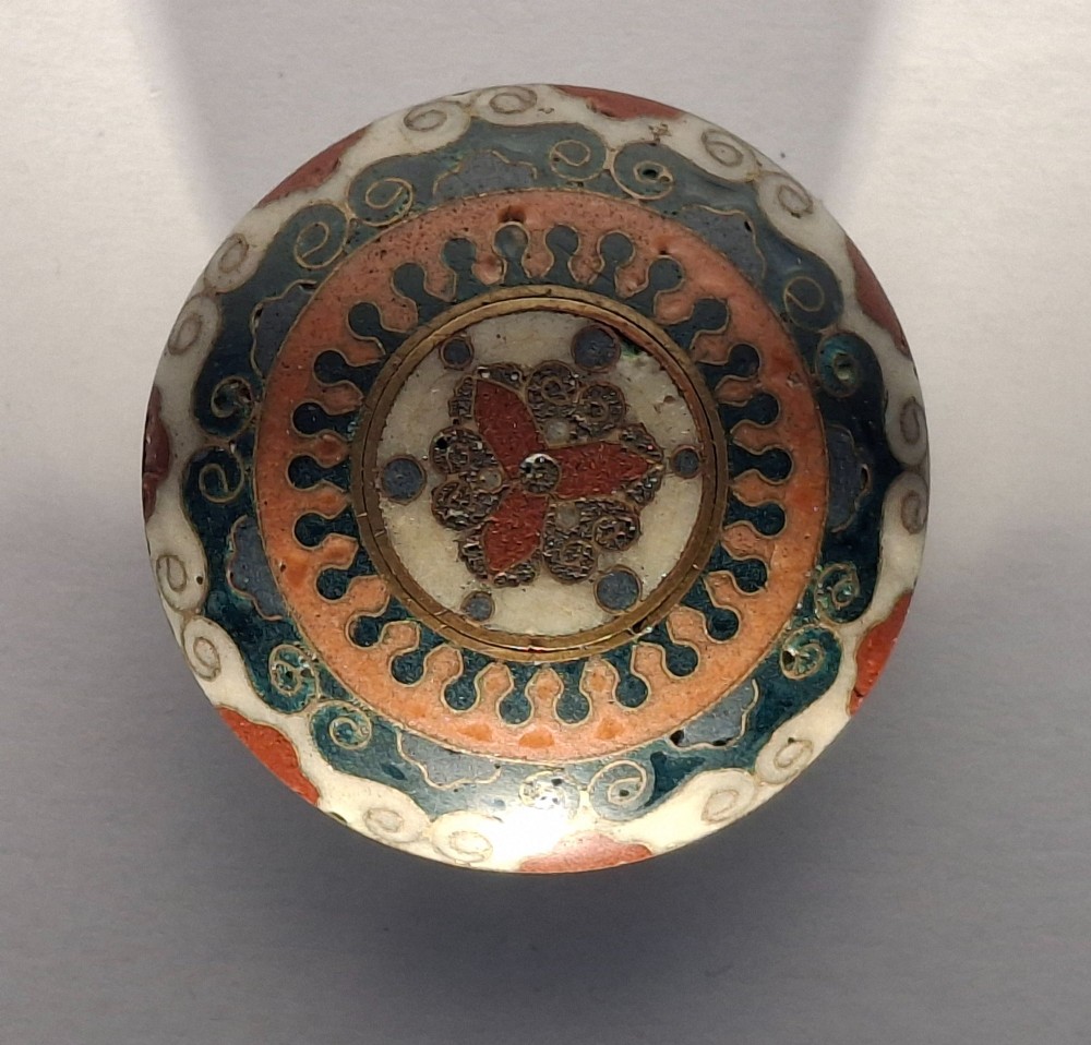 A circular Japanese manju netsuke in polychrome cloisonne enamel with central floral medallion and spiral border patterns. View V