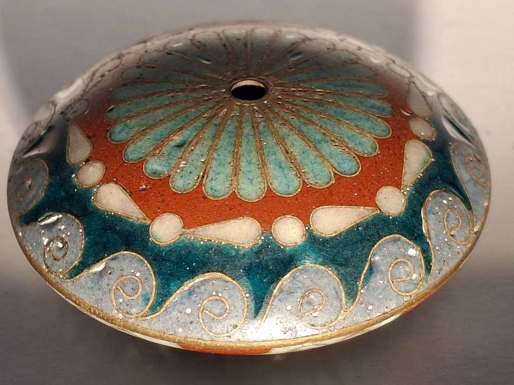 A circular Japanese manju netsuke in polychrome cloisonne enamel with central floral medallion and spiral border patterns. View VI