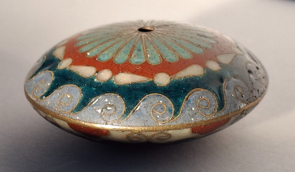 A circular Japanese manju netsuke in polychrome cloisonne enamel with central floral medallion and spiral border patterns. View VIII