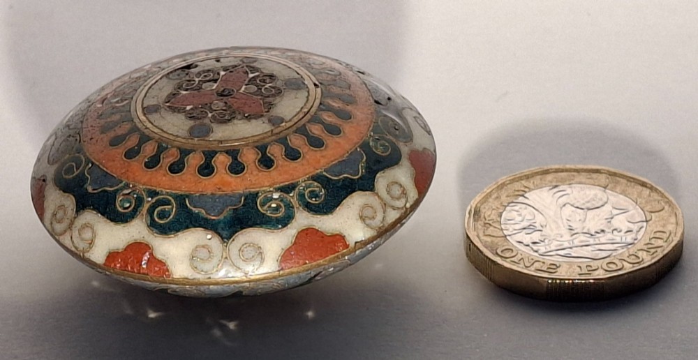 A circular Japanese manju netsuke in polychrome cloisonne enamel with central floral medallion and spiral border patterns. View X