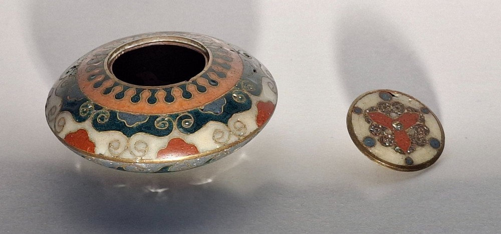 A circular Japanese manju netsuke in polychrome cloisonne enamel with central floral medallion and spiral border patterns. View XI
