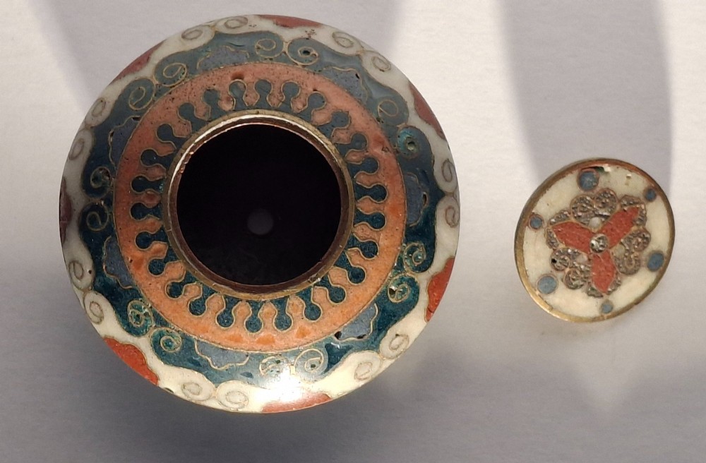 A circular Japanese manju netsuke in polychrome cloisonne enamel with central floral medallion and spiral border patterns. View XII