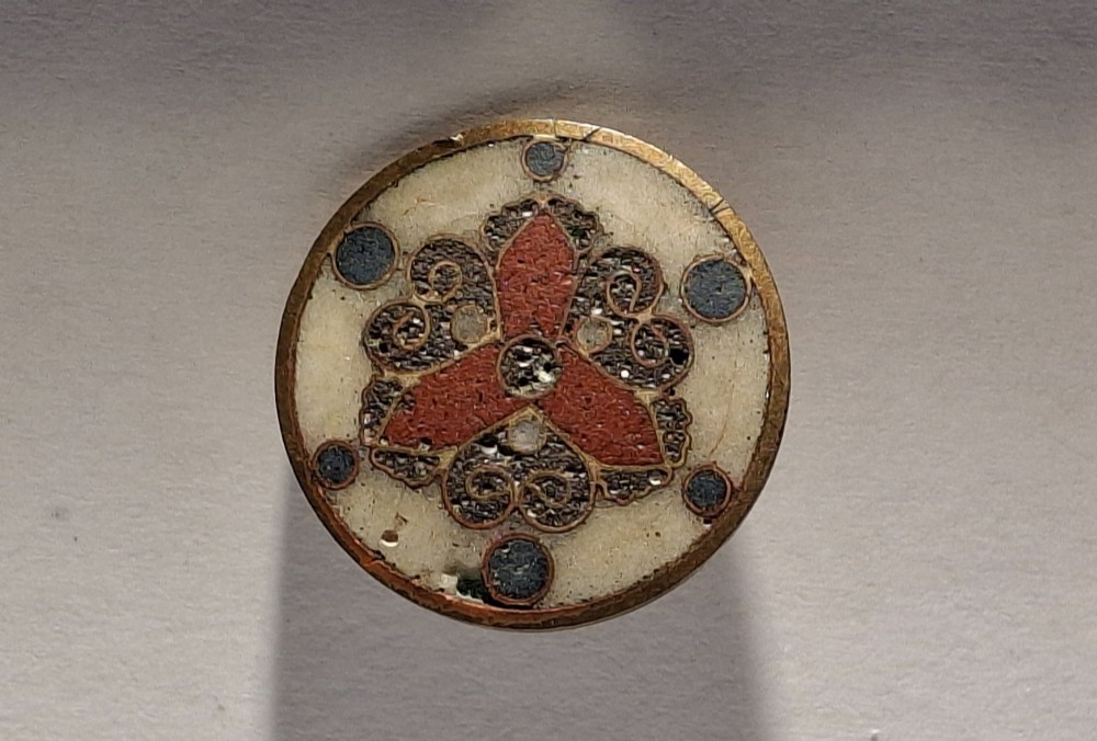 A circular Japanese manju netsuke in polychrome cloisonne enamel with central floral medallion and spiral border patterns. View XIV