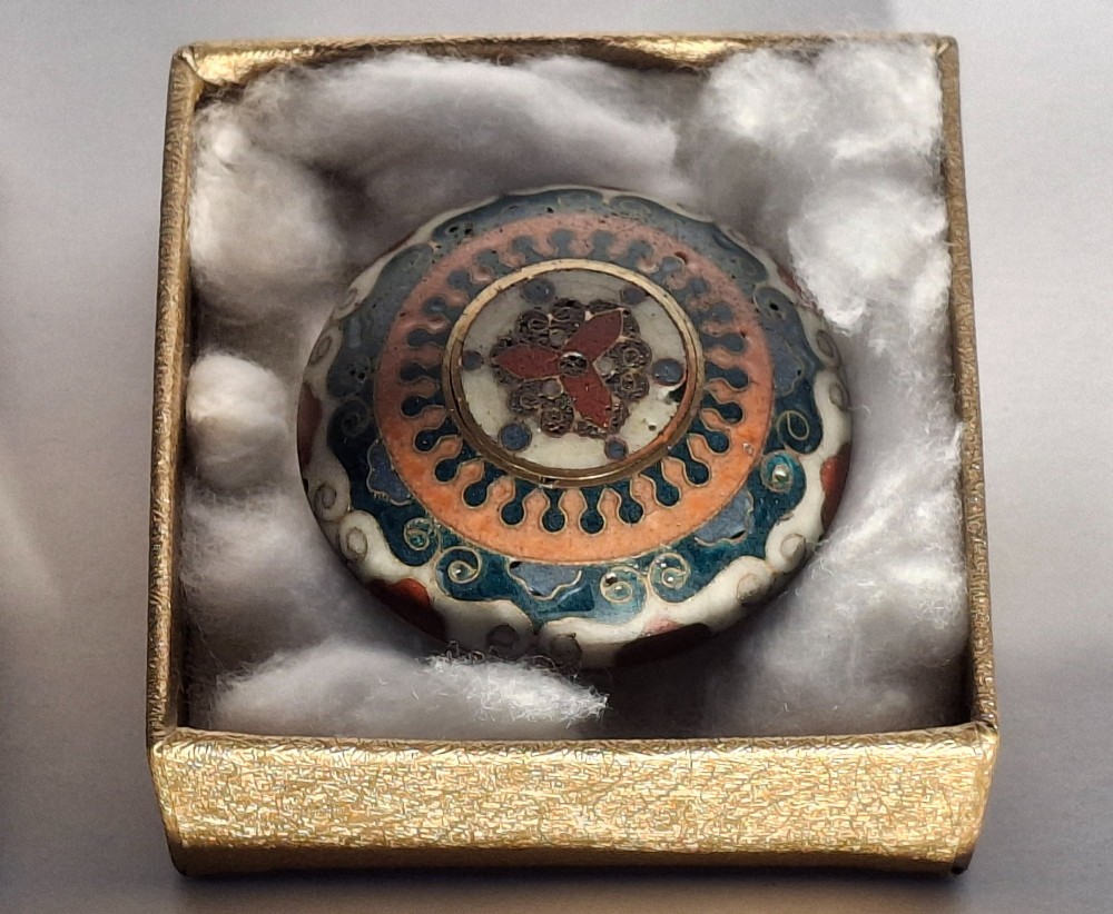A circular Japanese manju netsuke in polychrome cloisonne enamel with central floral medallion and spiral border patterns. View XV