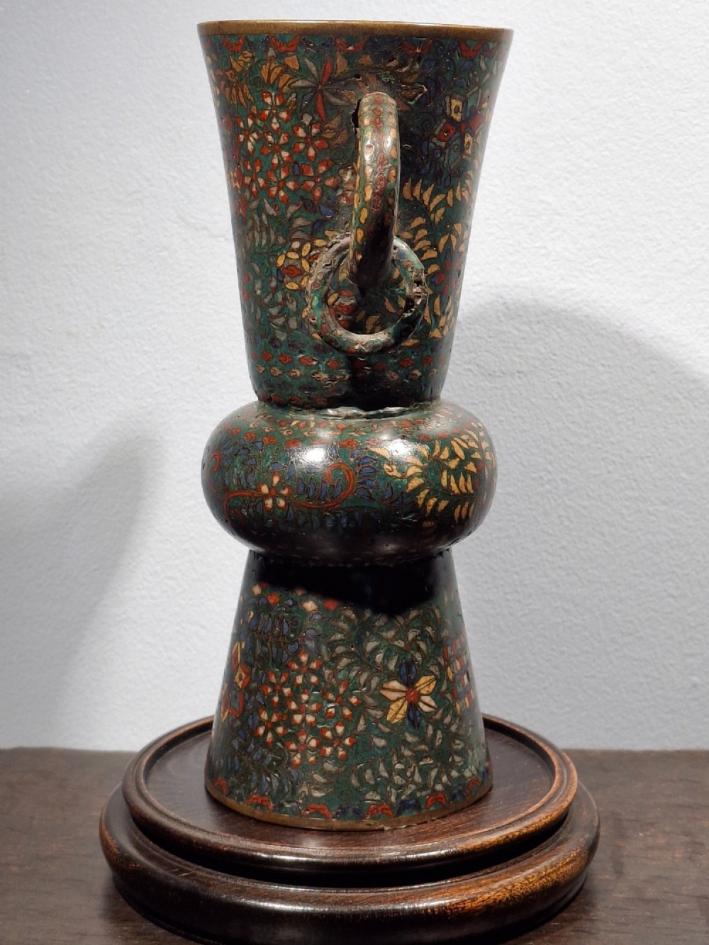 A miniature Japanese cloisonne enamel ritual vase with two loop handles, loose rings, and polychrome floral decoration on a dark green background. View II