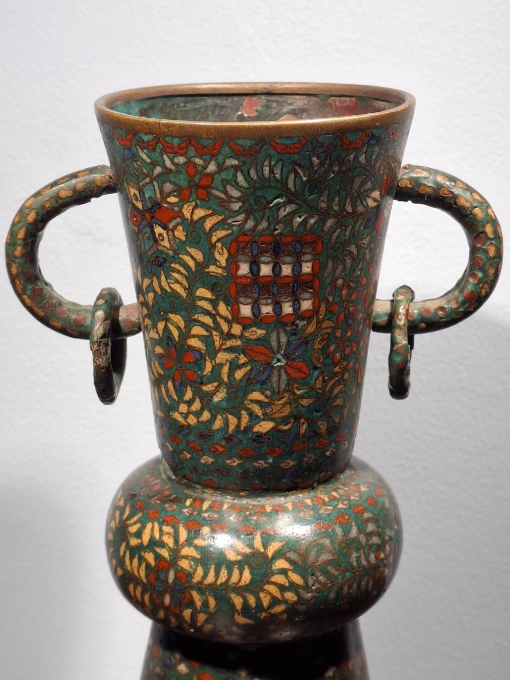 A miniature Japanese cloisonne enamel ritual vase with two loop handles, loose rings, and polychrome floral decoration on a dark green background. View IV