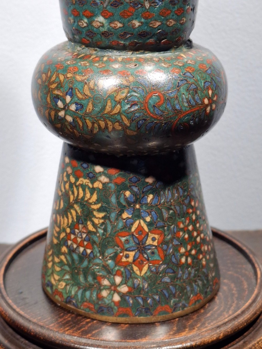 A miniature Japanese cloisonne enamel ritual vase with two loop handles, loose rings, and polychrome floral decoration on a dark green background. View VI