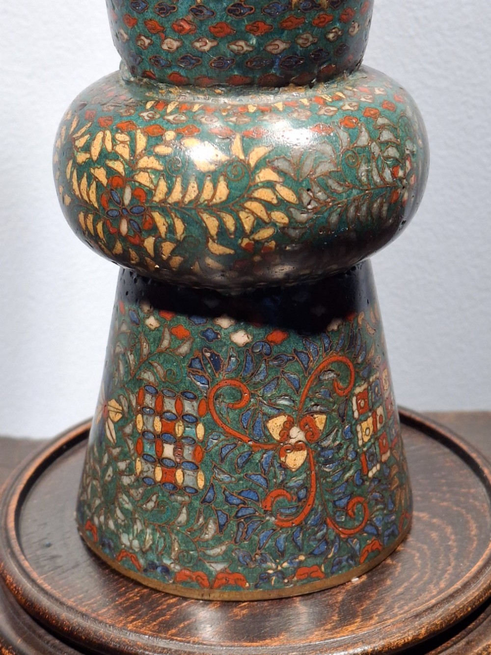 A miniature Japanese cloisonne enamel ritual vase with two loop handles, loose rings, and polychrome floral decoration on a dark green background. View VII