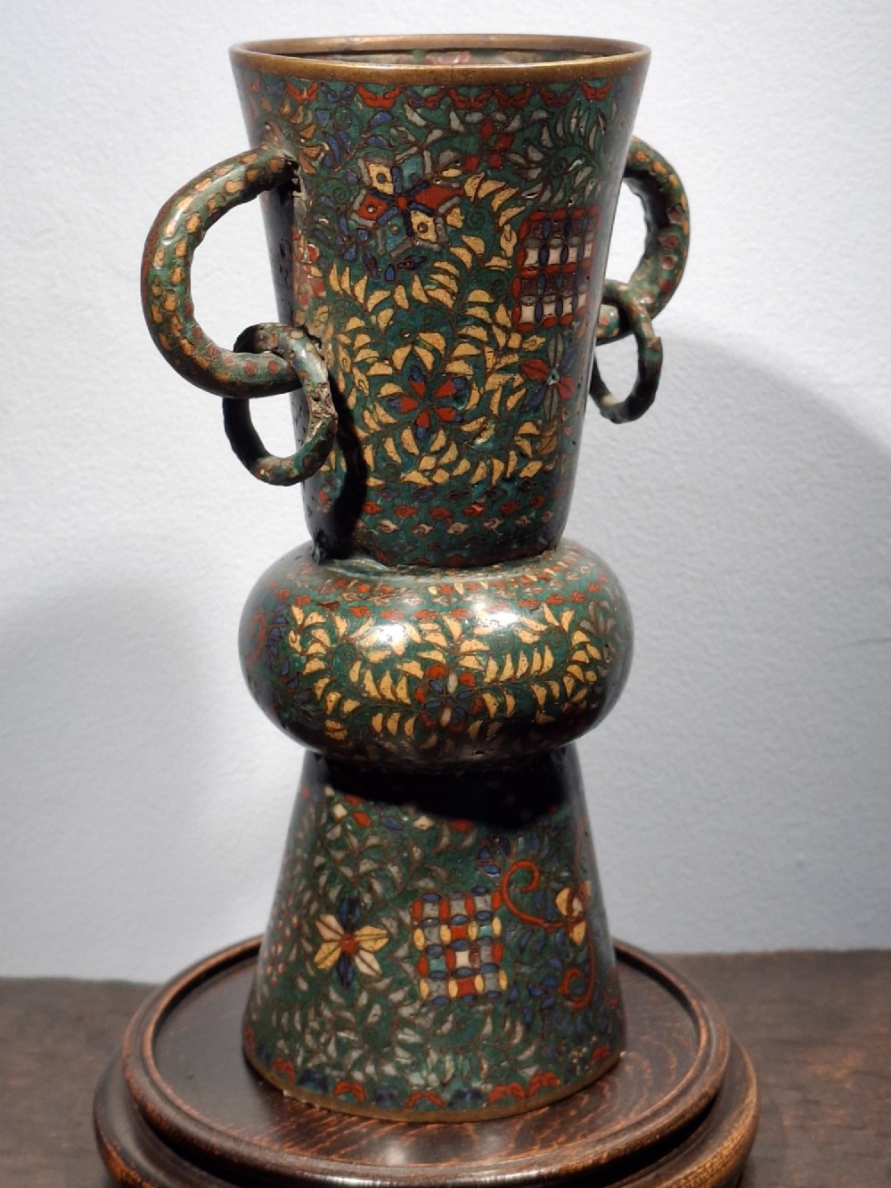 A miniature Japanese cloisonne enamel ritual vase with two loop handles, loose rings, and polychrome floral decoration on a dark green background. View XI