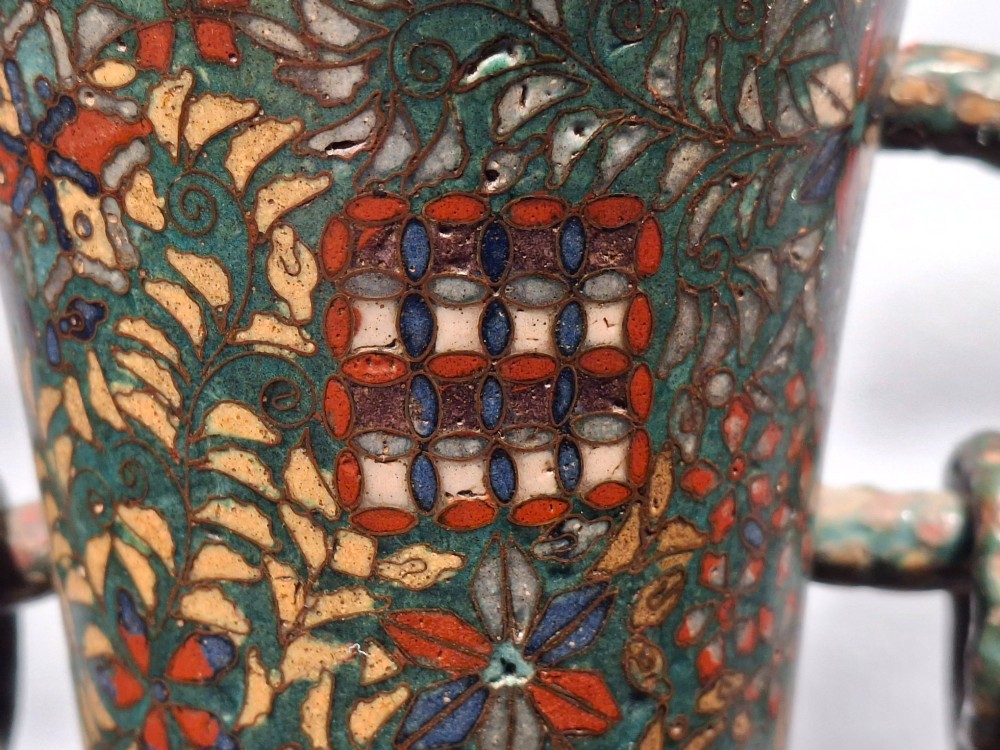 A miniature Japanese cloisonne enamel ritual vase with two loop handles, loose rings, and polychrome floral decoration on a dark green background. View XII