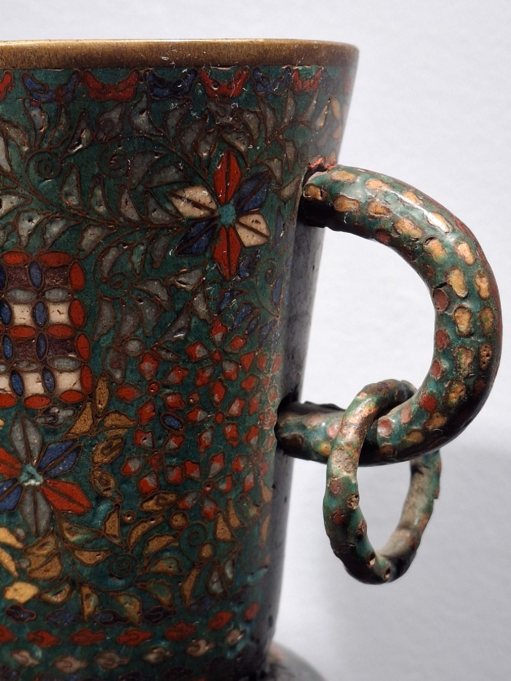 A miniature Japanese cloisonne enamel ritual vase with two loop handles, loose rings, and polychrome floral decoration on a dark green background. View XV