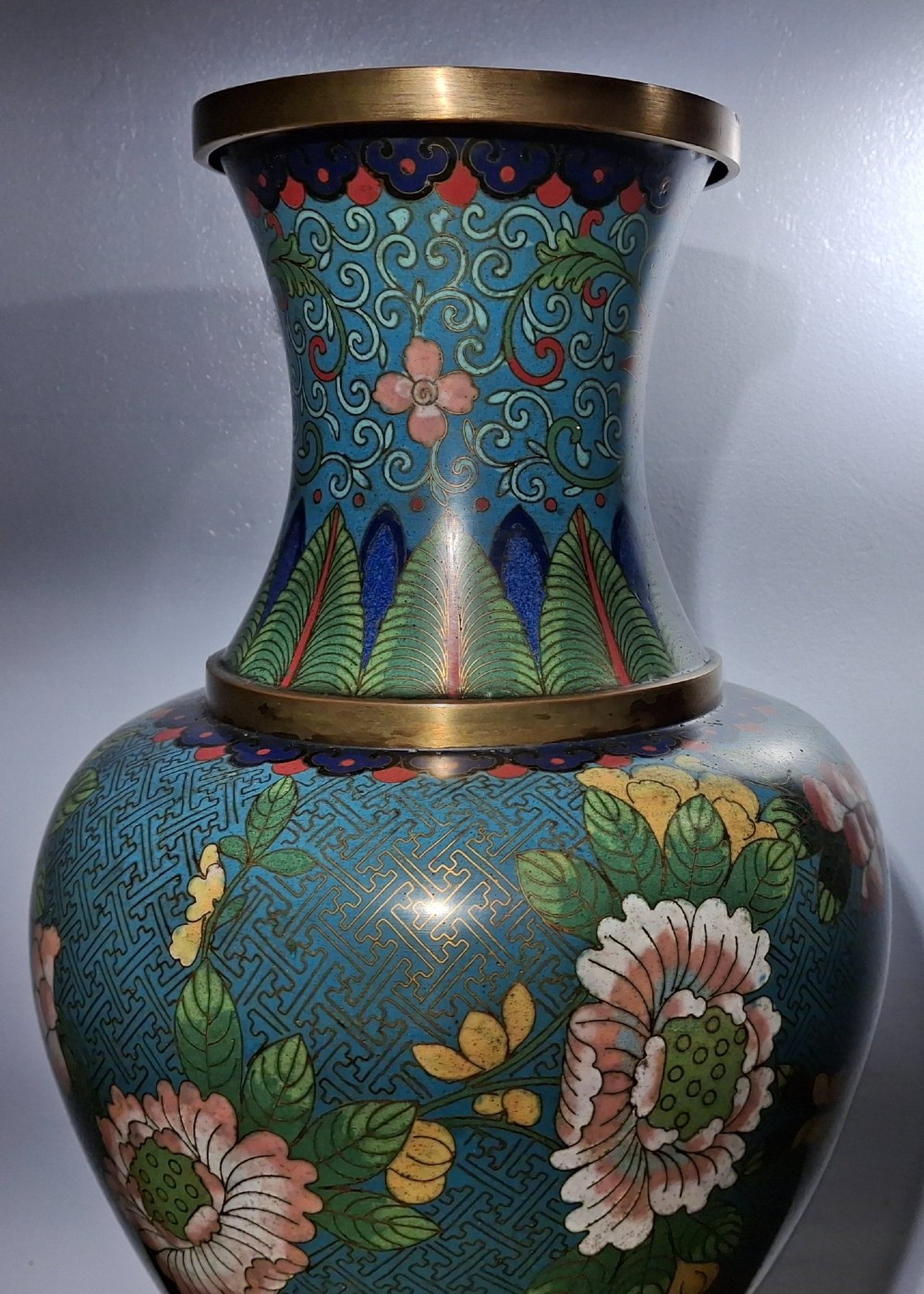 A large Chinese cloisonne enamel vase with pink and yellow floral motifs over a blue geometric ground and brass rim. View V