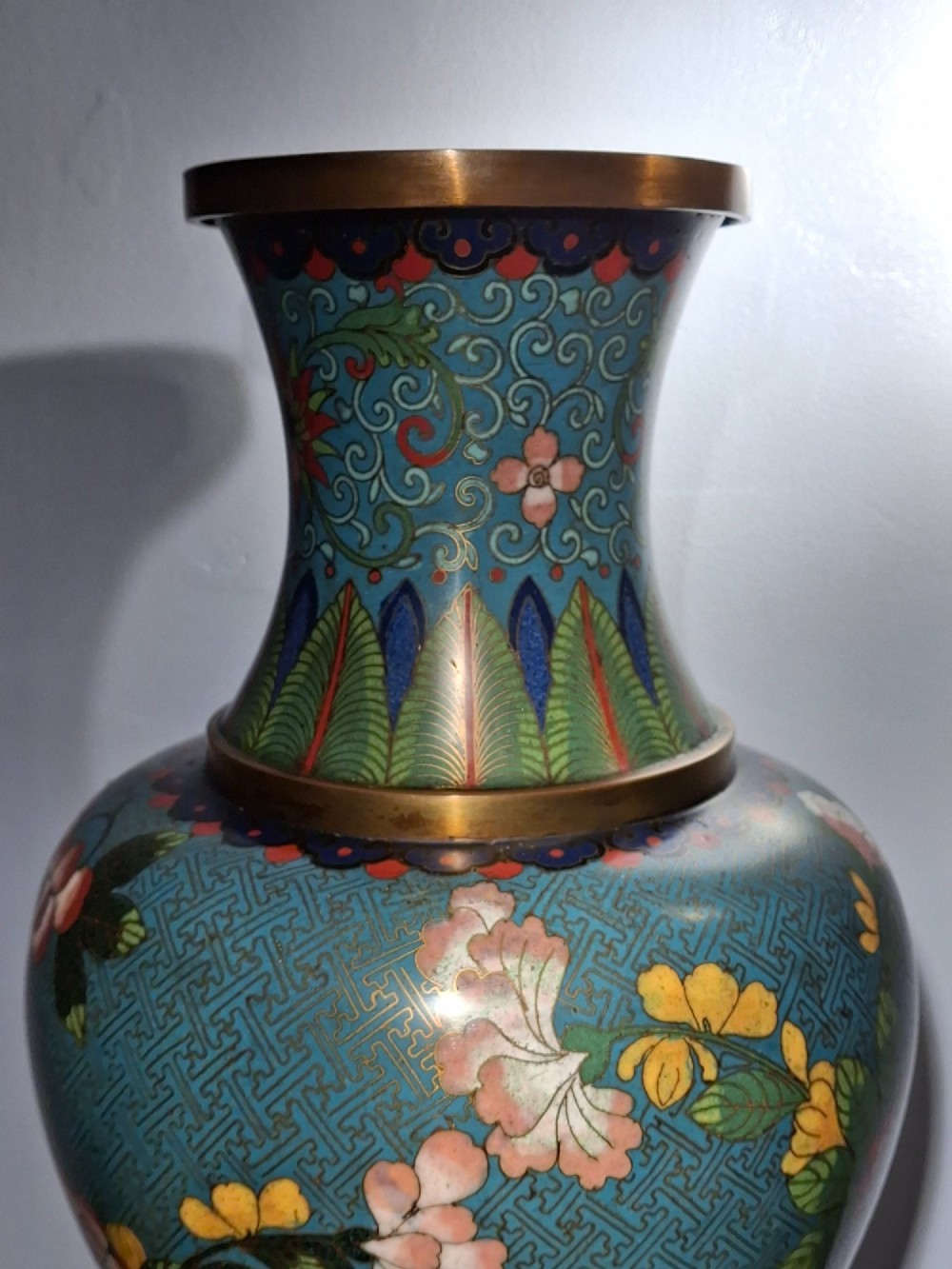 A large Chinese cloisonne enamel vase with pink and yellow floral motifs over a blue geometric ground and brass rim. View VII