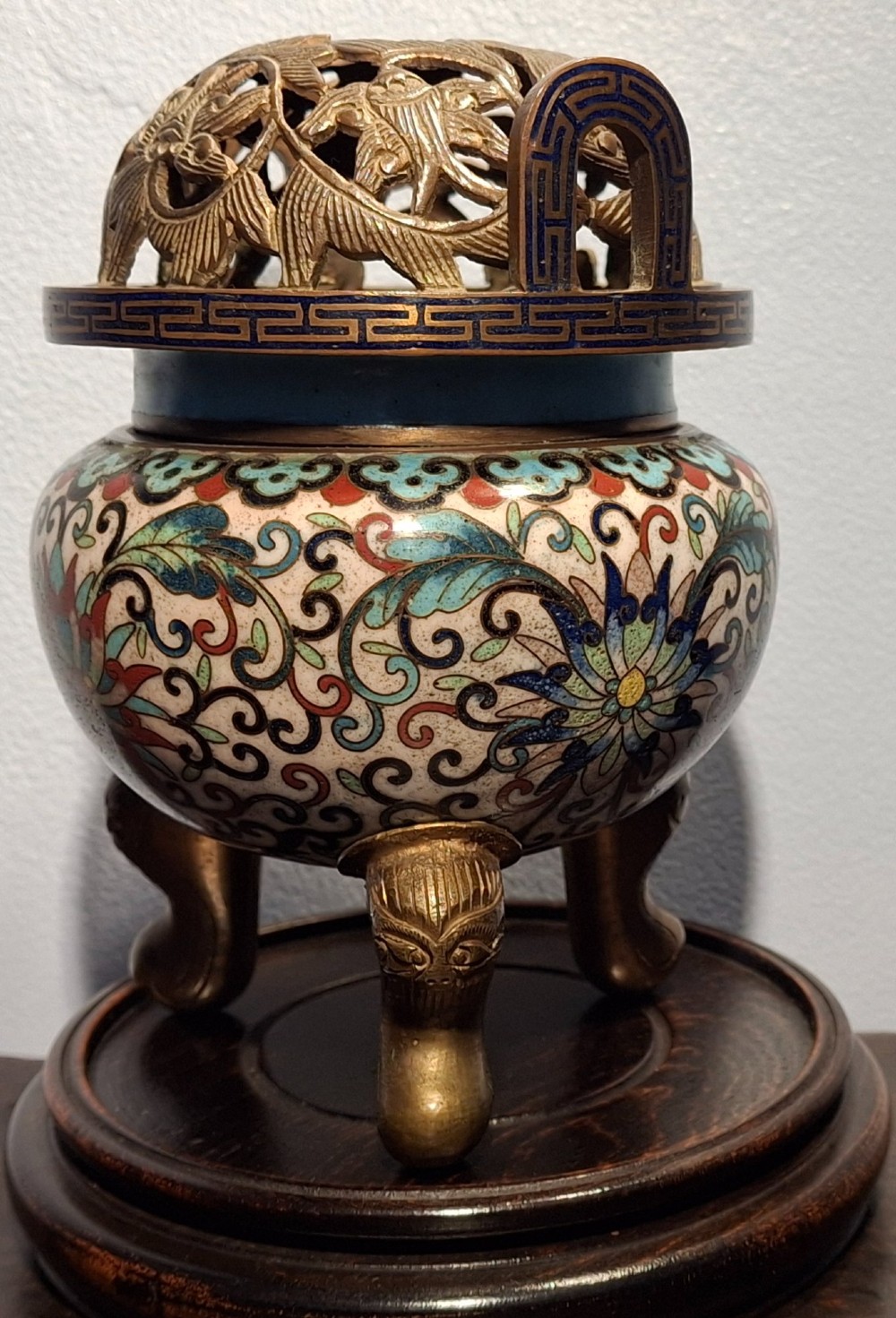 A 19th-century Chinese tripod cloisonne enamel censer featuring intricate floral scrollwork, upright loop handles, three gilded cabriole feet, and a pierced brass cover. View IV