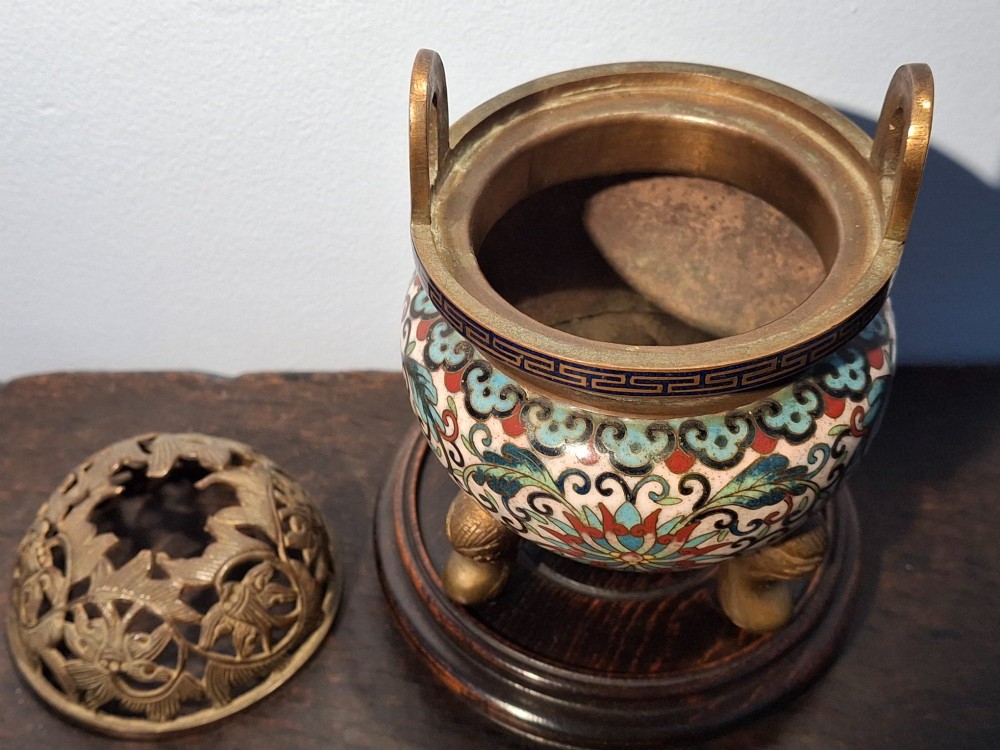 A 19th-century Chinese tripod cloisonne enamel censer featuring intricate floral scrollwork, upright loop handles, three gilded cabriole feet, and a pierced brass cover. View IX