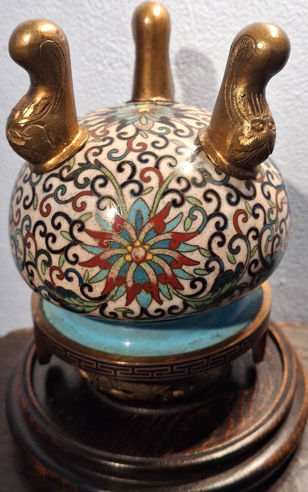 A 19th-century Chinese tripod cloisonne enamel censer featuring intricate floral scrollwork, upright loop handles, three gilded cabriole feet, and a pierced brass cover. View X