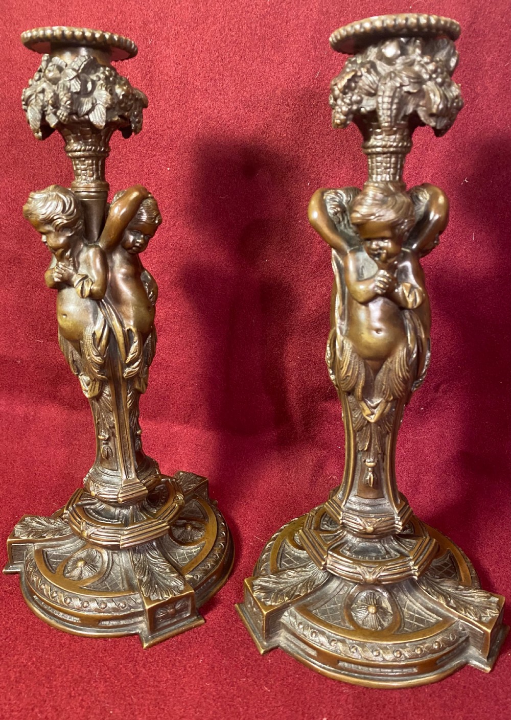 A pair of cast patinated bronze candlesticks featuring stems sculpted with putti figures and ornate stepped bases decorated with acanthus motifs.