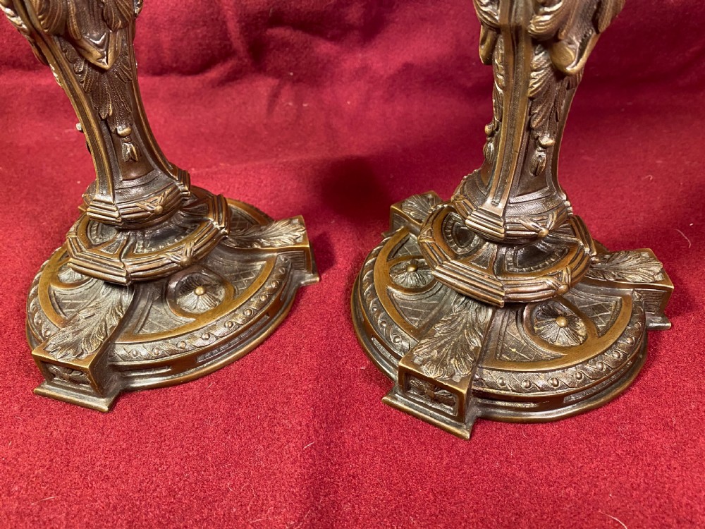 A pair of cast patinated bronze candlesticks featuring stems sculpted with putti figures and ornate stepped bases decorated with acanthus motifs. View X