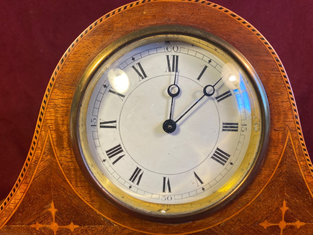 An Edwardian satinwood mantel clock featuring an arched case with geometric cross marquetry, a white Roman numeral dial, and a brass bezel. View II