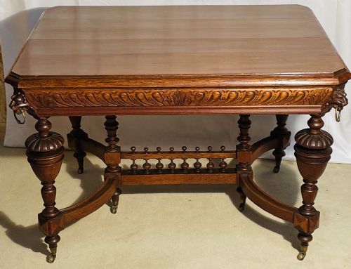 fig 1. A Victorian Gothic honey oak centre table featuring carved aprons, corner lion mask motifs with brass rings, turned legs, and an arched cross-stretcher base on castors.