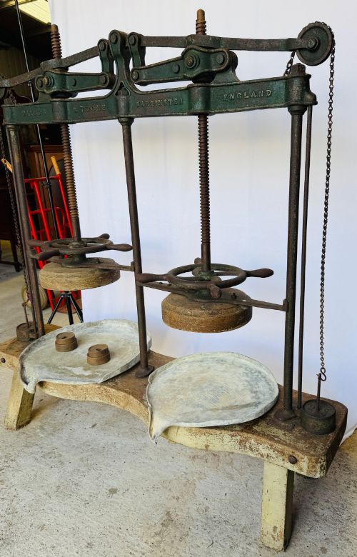 fig 1. A Victorian double cheese press with a painted dark green cast-iron upper frame, twin screw spindles, and a heavy wooden base structure.