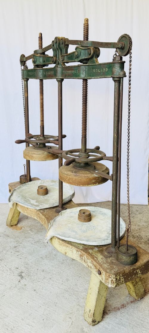 A Victorian double cheese press with a painted dark green cast-iron upper frame, twin screw spindles, and a heavy wooden base structure. View VII
