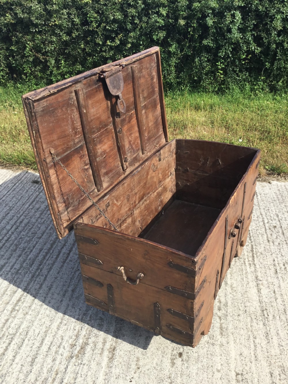 A mid-19th-century colonial wooden strong box featuring wrought iron straps, a central clasp, corner brackets, and large wooden wheels. View VII
