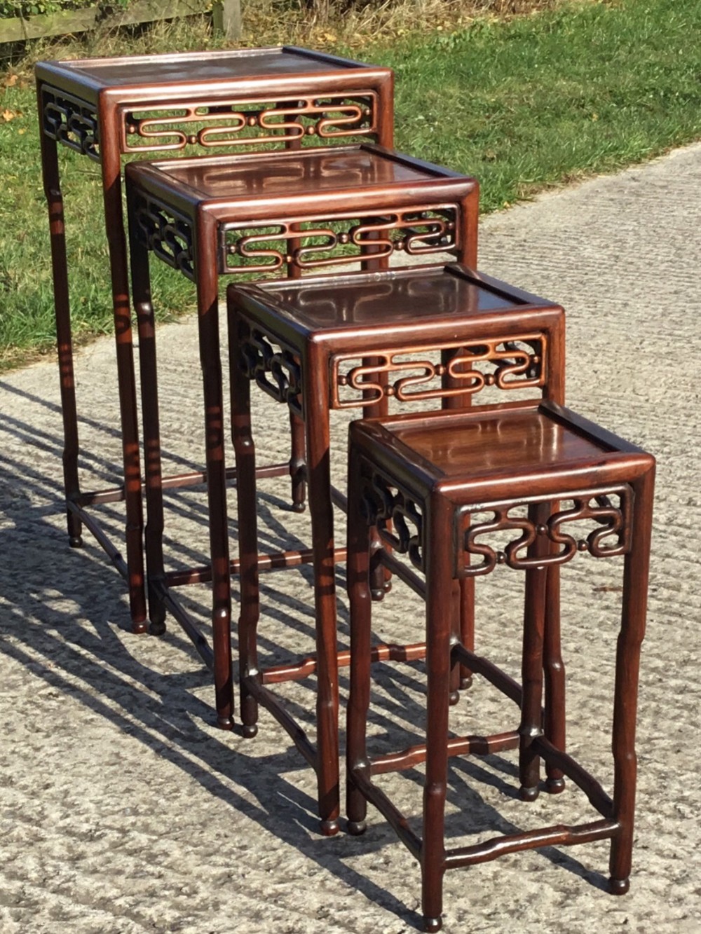 A set of four graduating Chinese rosewood nesting tables featuring reticulated carved aprons and slender legs.