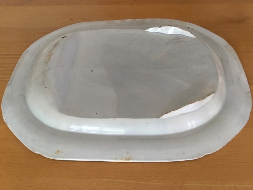 An oval blue and white pearlware platter featuring a printed pastoral scene with sheep, a musician figure, a floral border, and a gravy reservoir well. View VII