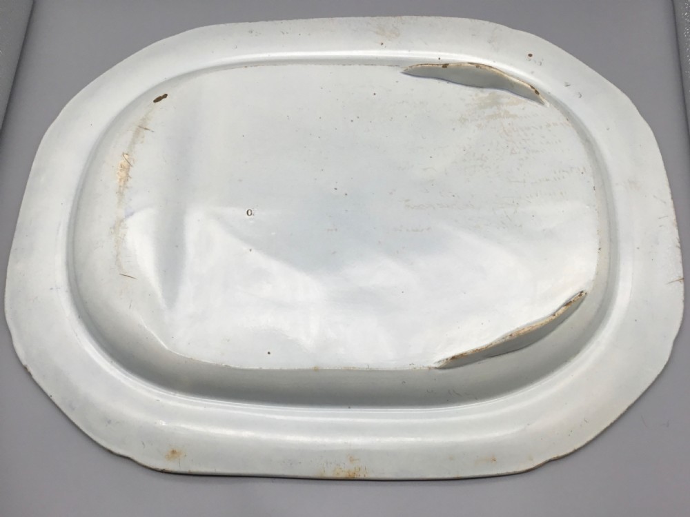 An oval blue and white pearlware platter featuring a printed pastoral scene with sheep, a musician figure, a floral border, and a gravy reservoir well. View XI