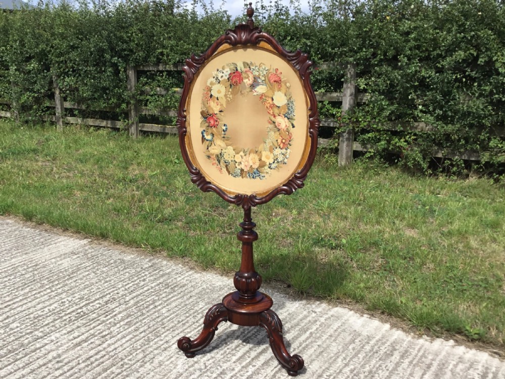 An antique Victorian rosewood pole screen featuring a carved oval frame with a floral wreath needlepoint panel, supported on a turned column with a tripod cabriole base. View V