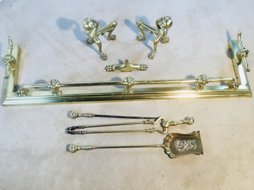 A polished brass fireside suite including a fender, two fire dogs with claw and ball feet, and three matching companion tools.