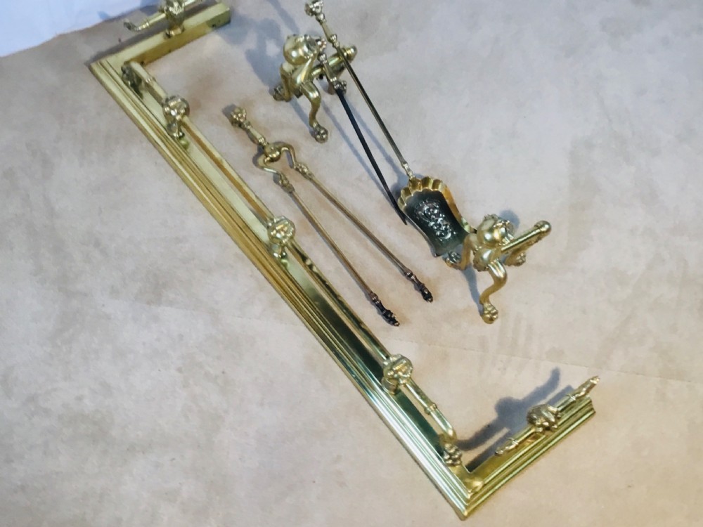 A polished brass fireside suite including a fender, two fire dogs with claw and ball feet, and three matching companion tools. View XV