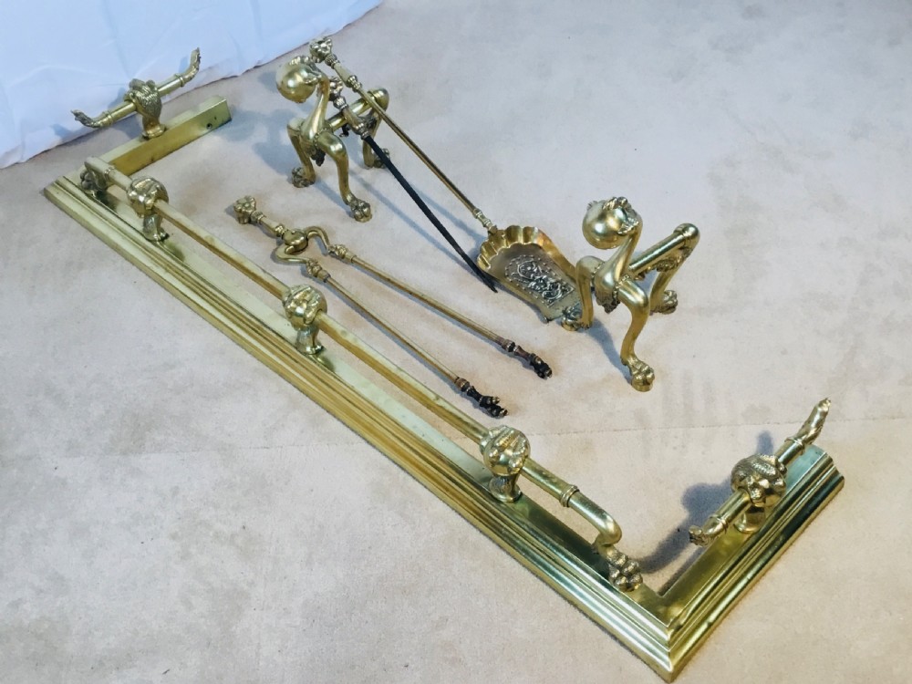 A polished brass fireside suite including a fender, two fire dogs with claw and ball feet, and three matching companion tools. View XVI