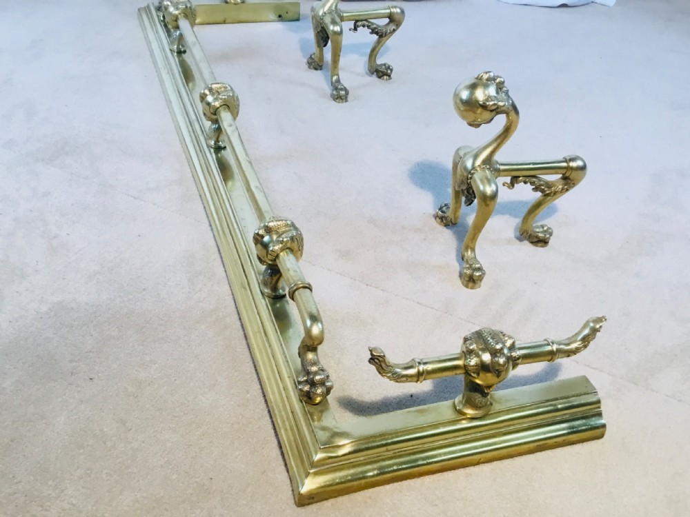 A polished brass fireside suite including a fender, two fire dogs with claw and ball feet, and three matching companion tools. View XVII