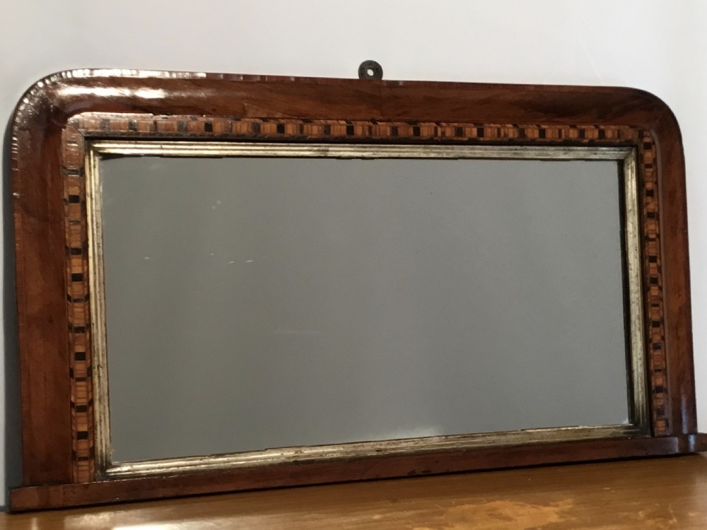 A Victorian walnut overmantel mirror featuring a low rectangular frame with rounded top corners, detailed geometric wood inlay, and a gilded inner slip surrounding a reflective mirror plate.
