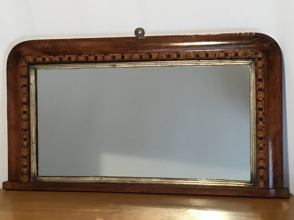 A Victorian walnut overmantel mirror featuring a low rectangular frame with rounded top corners, detailed geometric wood inlay, and a gilded inner slip surrounding a reflective mirror plate. View III